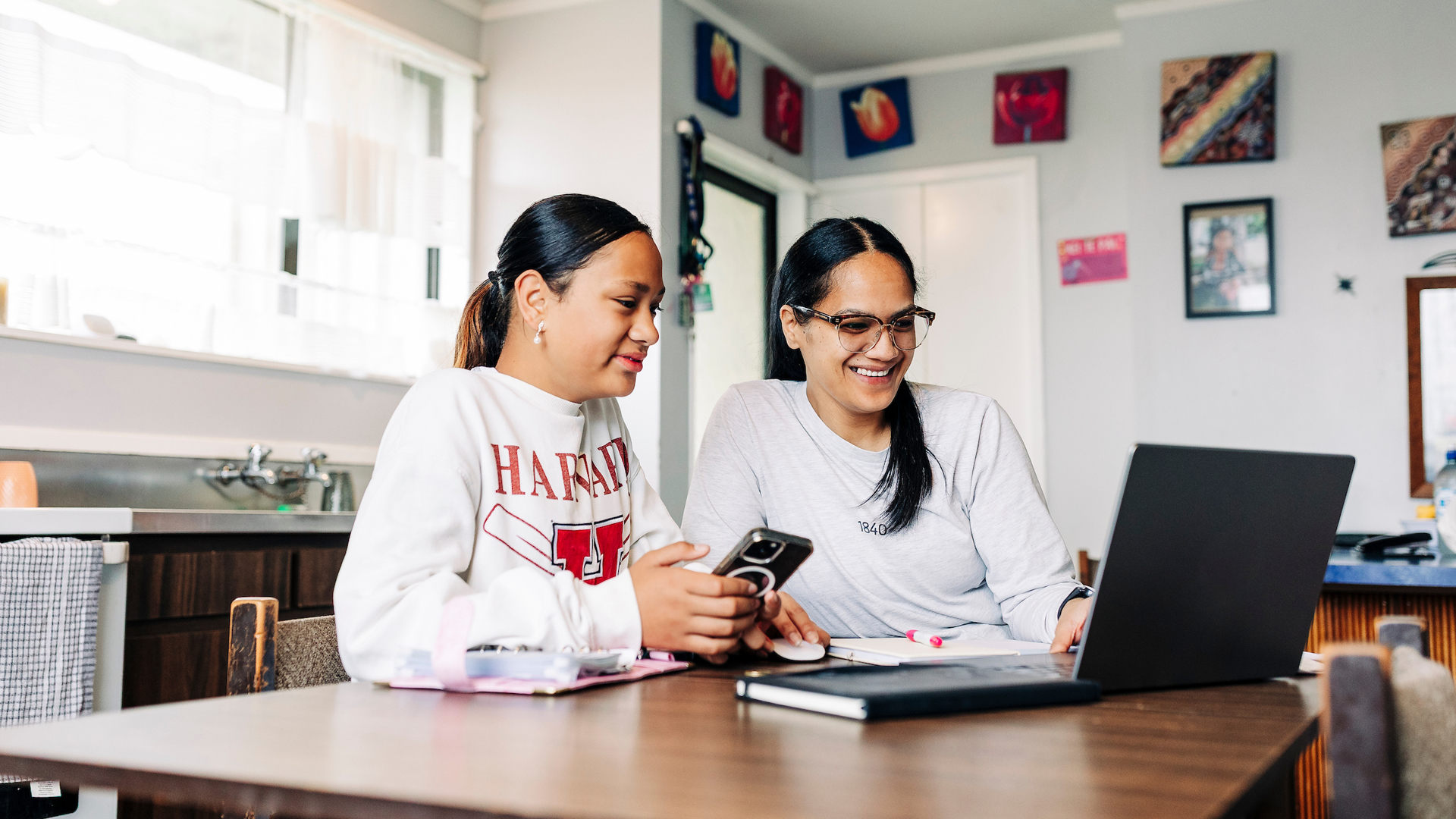 A woman and a teenage girl using a laptop at the dining table